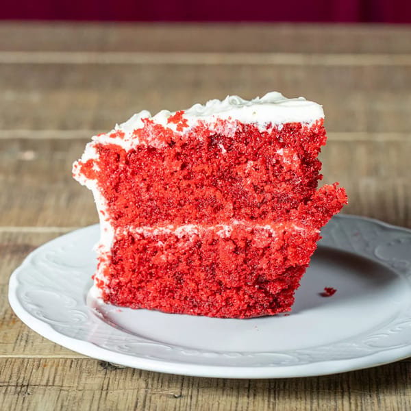 A slice of J's Eatery's red velvet cake with white frosting on a white plate.