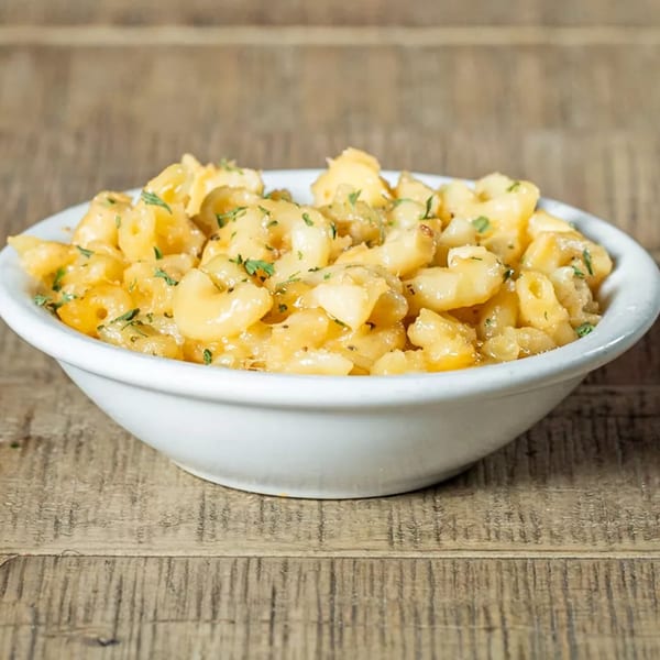 A white bowl of J's Eatery's soul-food macaroni and cheese, garnished with parsley, on a wooden table.