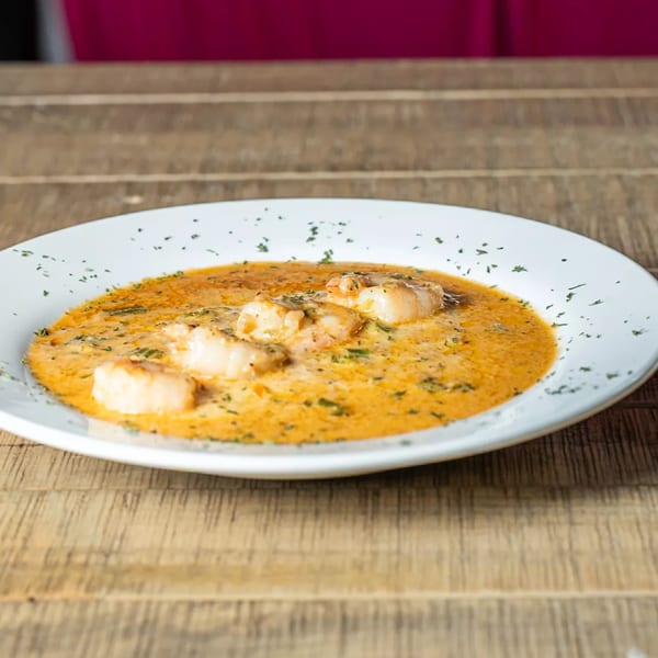 J's Eatery's soul-food shrimp and grits, a creamy orange dish with green herbs, on a wooden table.