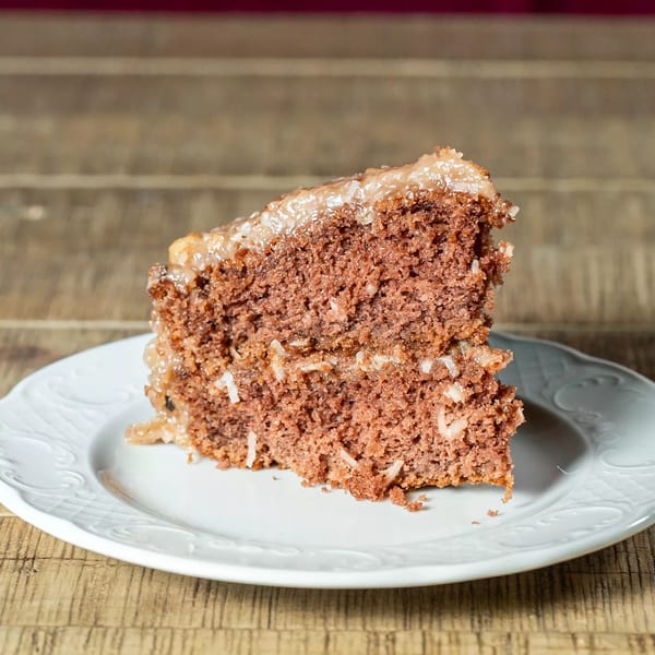 A slice of J's Eatery's German chocolate cake with coconut pecan frosting on a white plate.