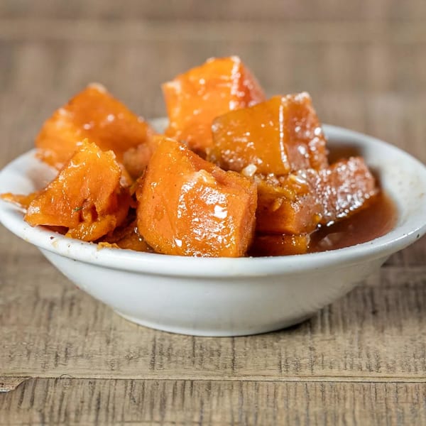 A white bowl filled with J's Eatery's candied yams, glistening with syrup and sugar crystals.