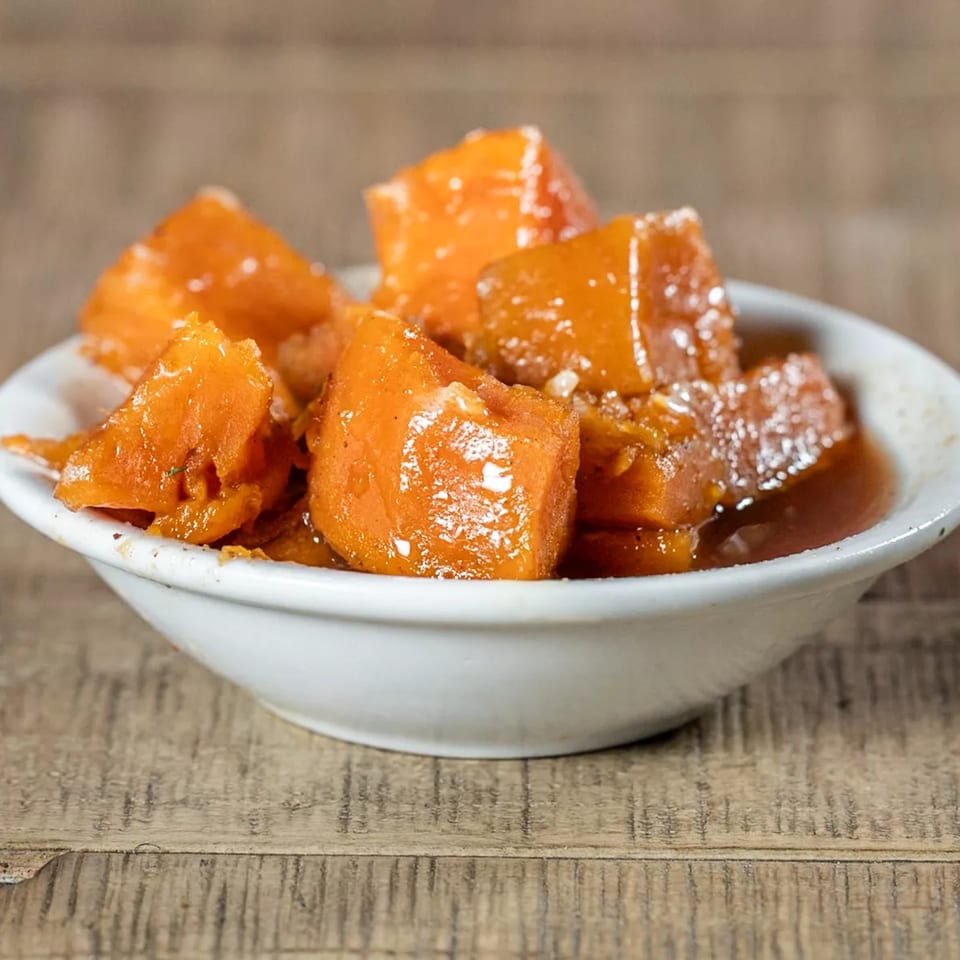 A white bowl filled with J's Eatery's candied yams, glistening with syrup and sugar crystals.