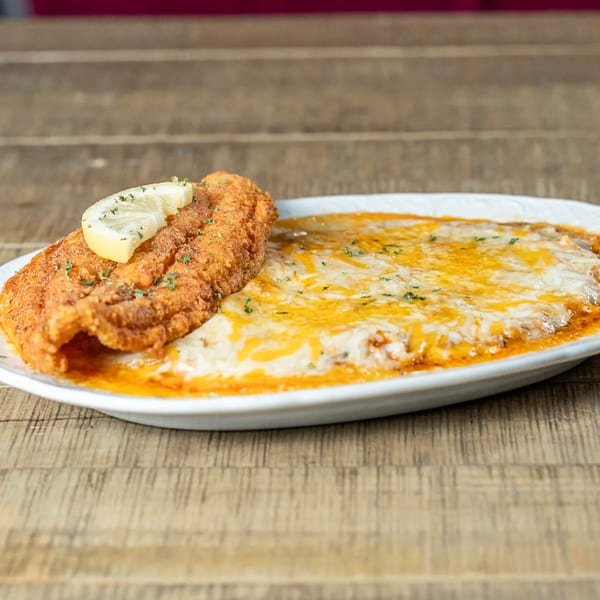 J's Eatery's fried catfish with a lemon slice, served alongside cheesy grits on a white plate.